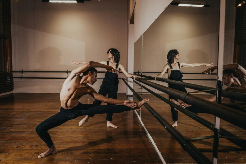 Two ballet dancers perform flexible poses during rehearsal in a dance studio.